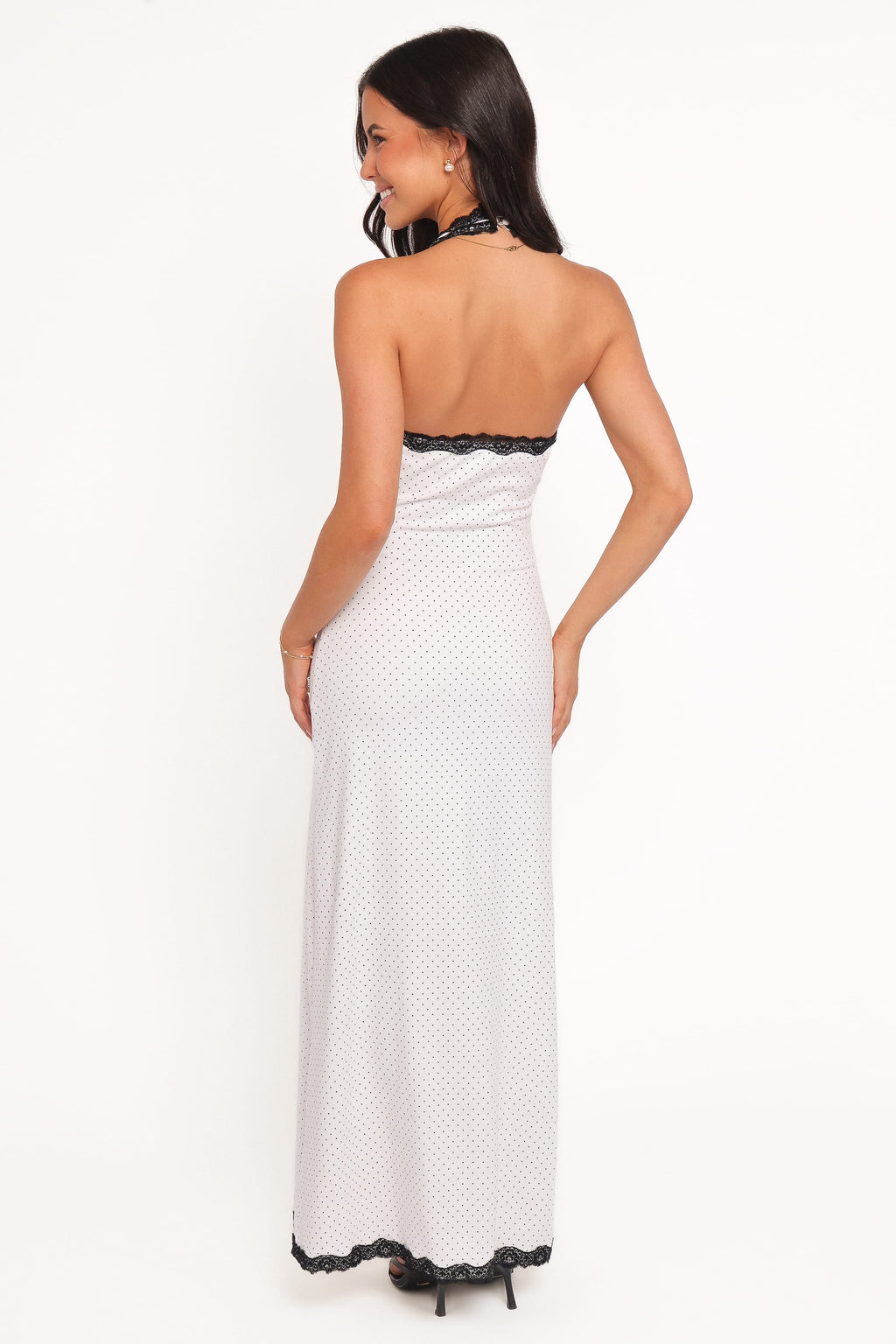 Woman wearing a white polka dot dress with black lace trim on a white background