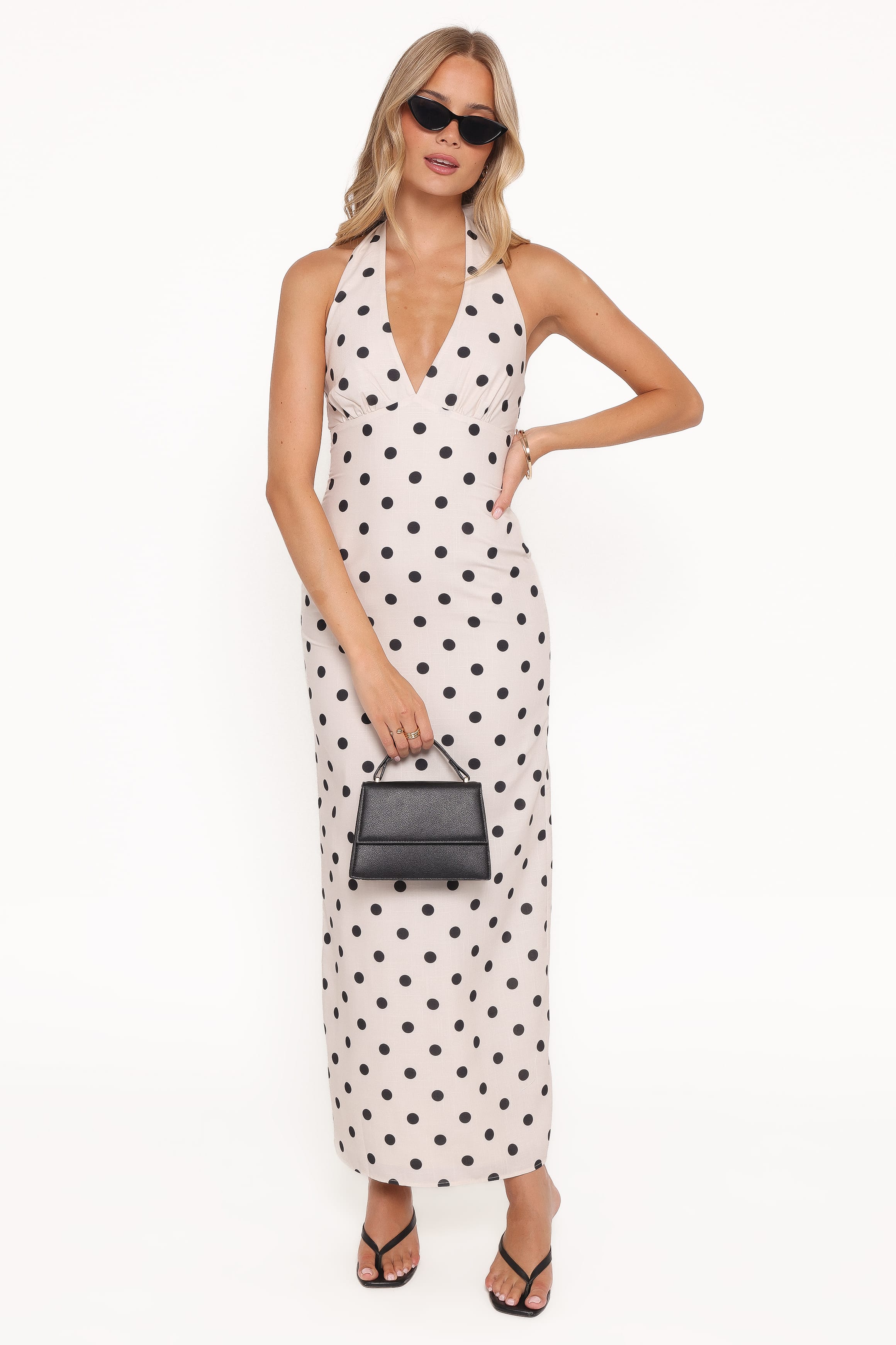 Woman wearing a white dress with black polka dots and holding a black handbag on a white background