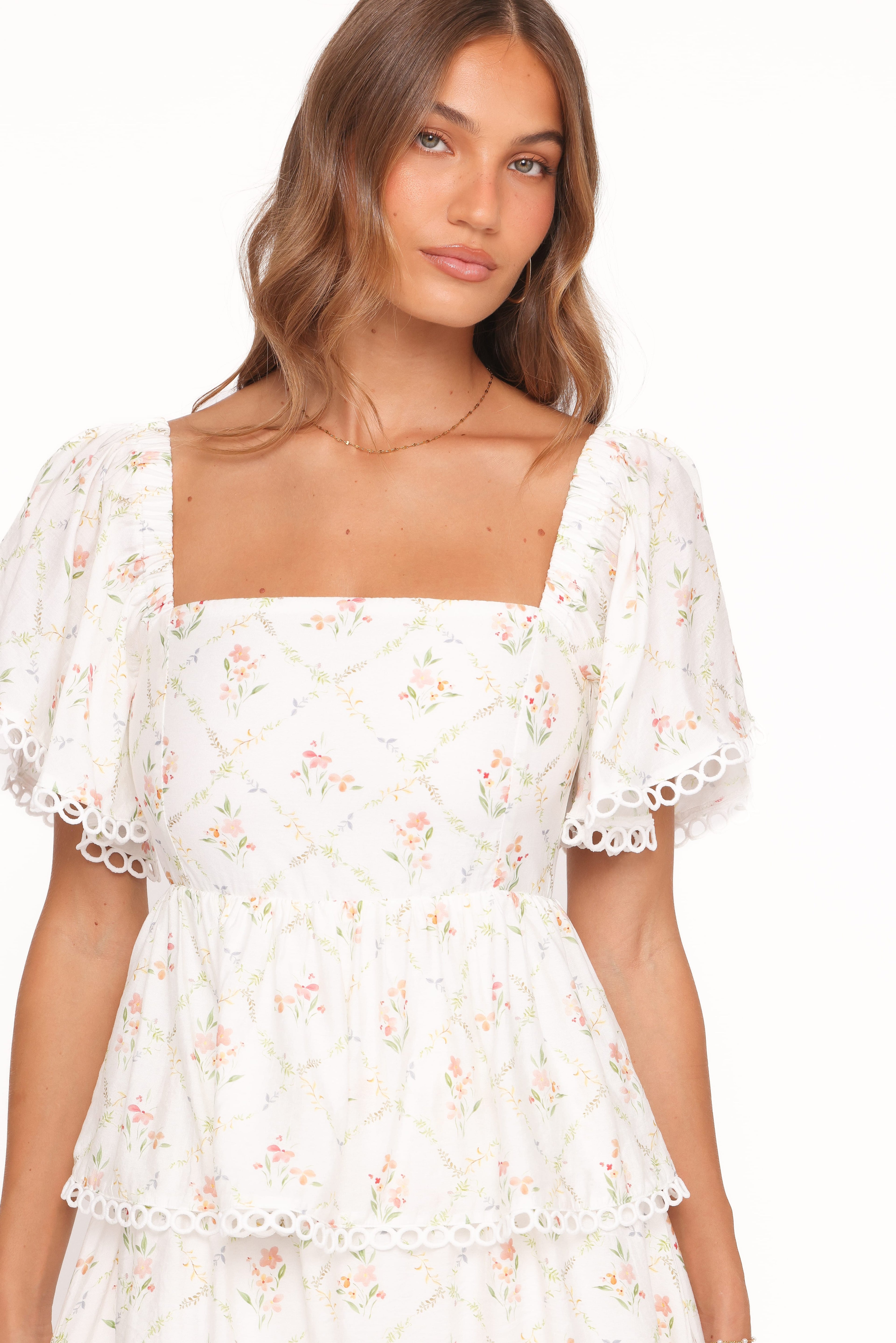 Woman wearing a white floral dress on a plain background