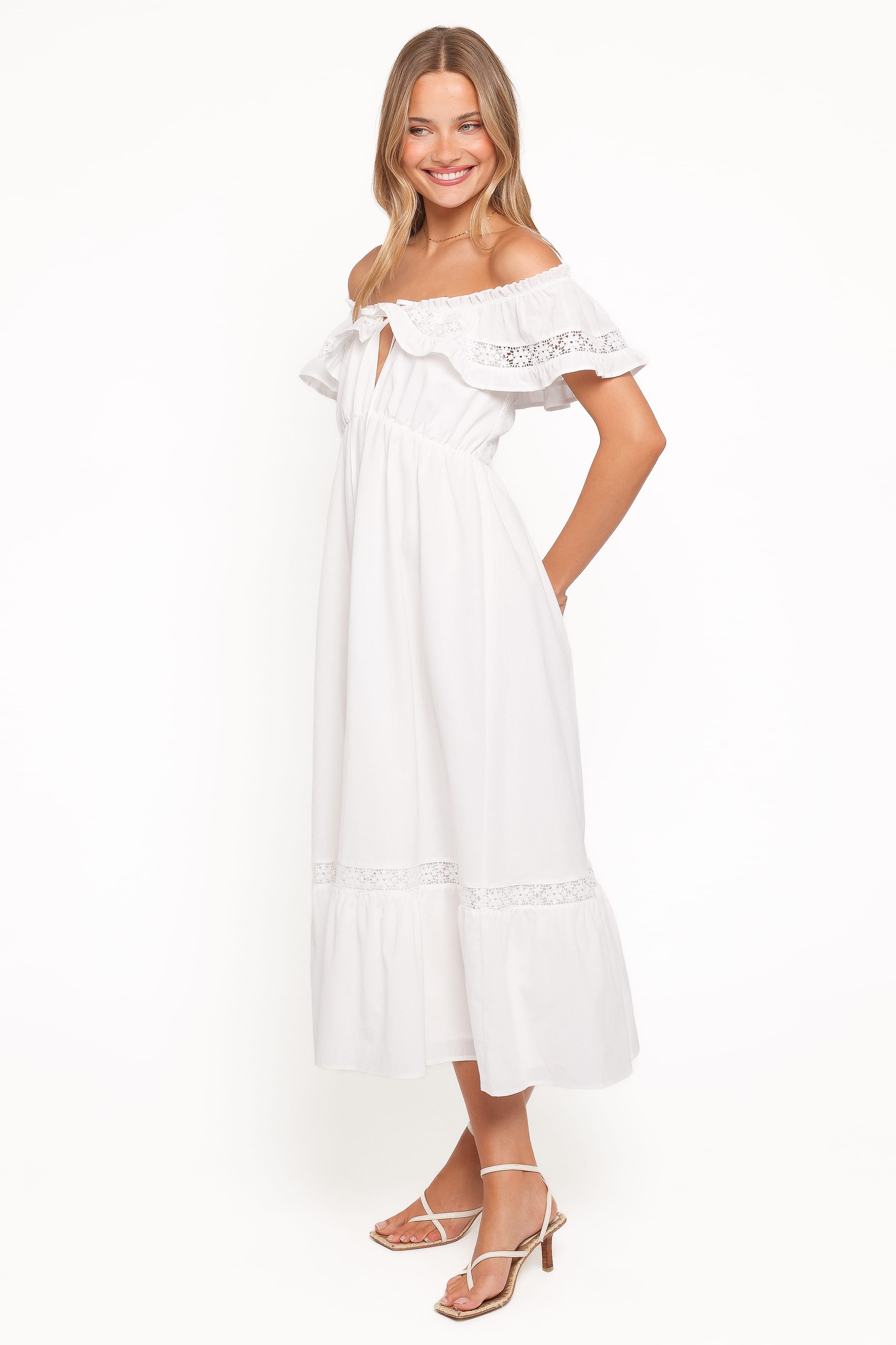 Woman wearing a white off-shoulder dress with lace details on a white background
