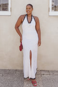Woman in a white dress with black trim standing against a beige wall.