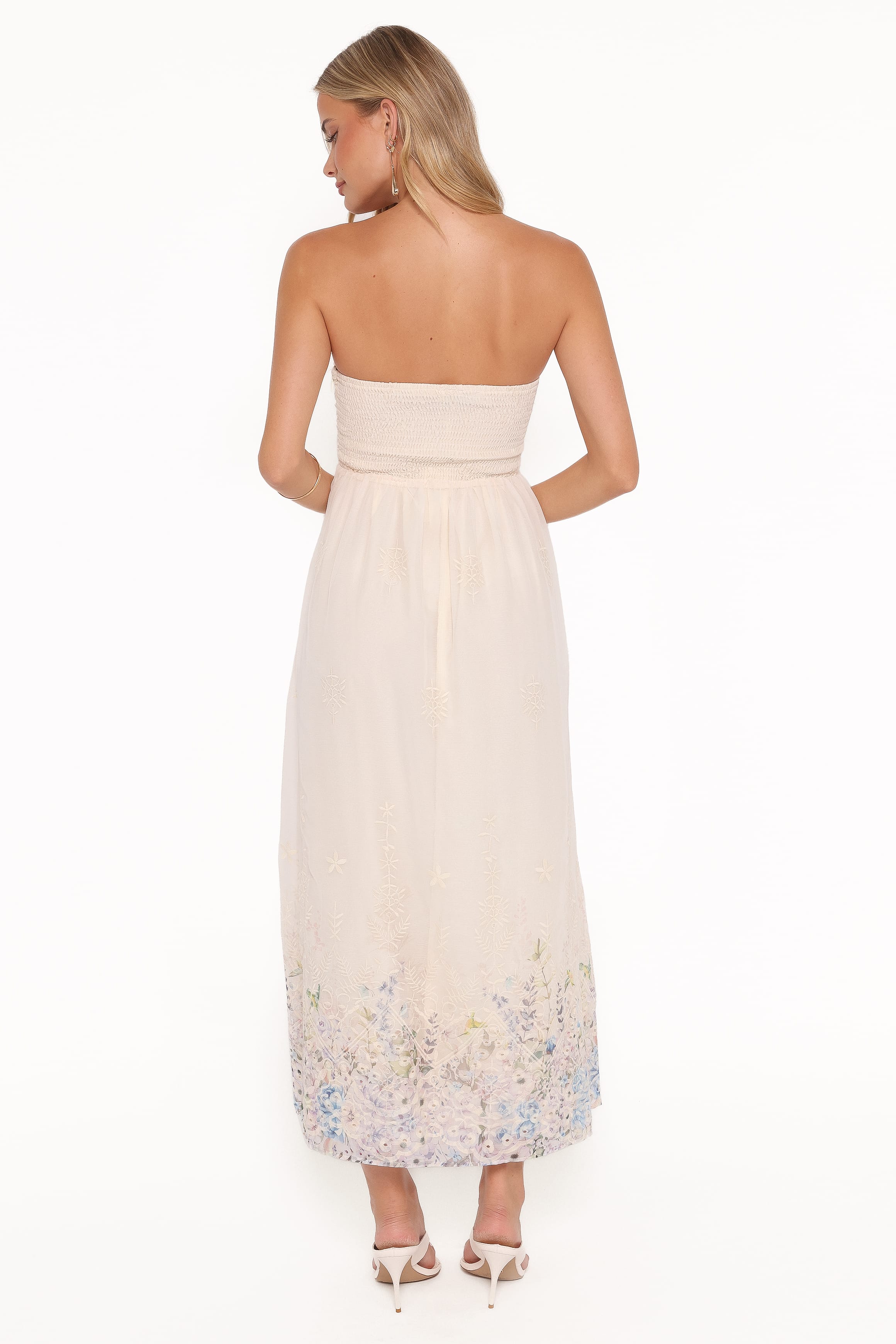 Woman wearing a strapless white dress with floral embroidery on a white background