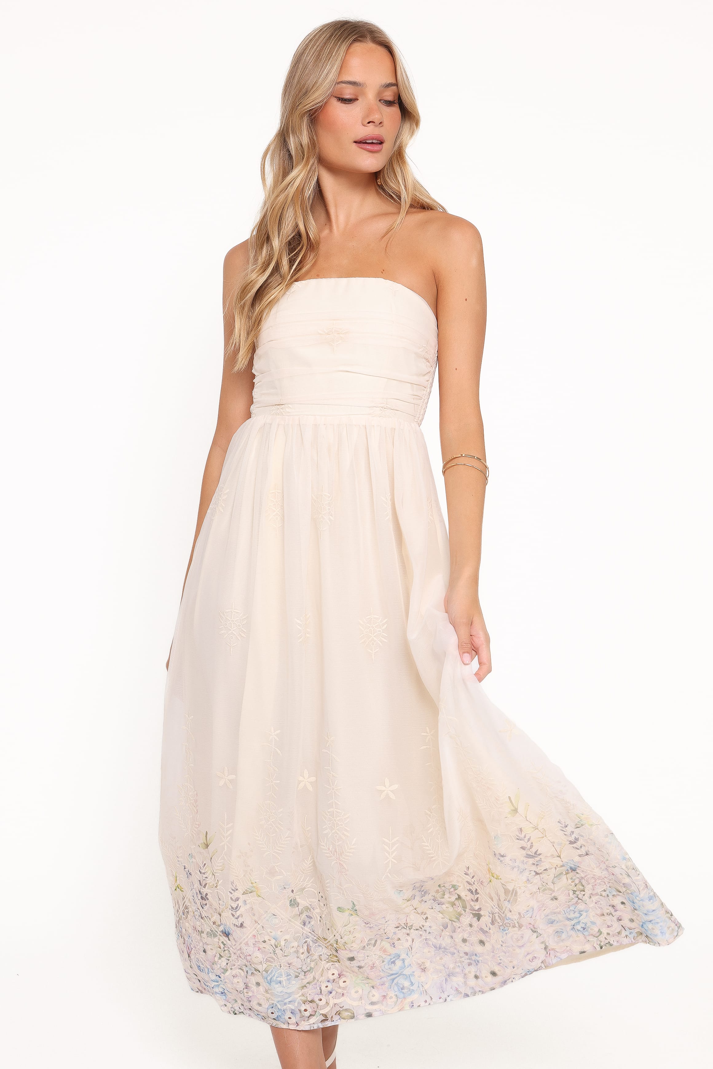 Woman wearing a strapless white dress with floral embroidery on a white background